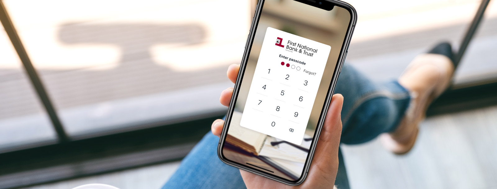 Woman holding a mobile device with First National Bank & Trust digital banking login screen.