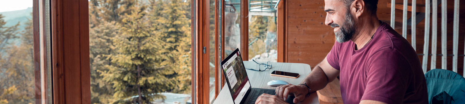 Man exploring First National Bank & Trust website with wooded view