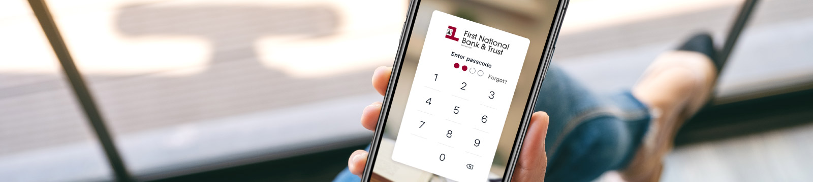 Woman holding a mobile device with First National Bank & Trust digital banking login screen.